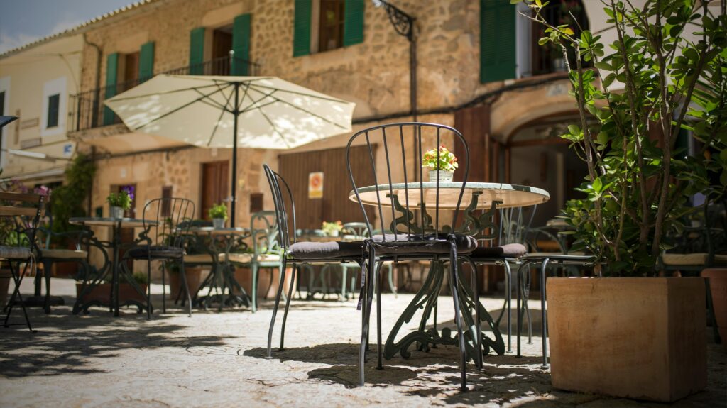 A quaint outdoor café in Mallorca, Spain, with iron chairs and rustic stone buildings.